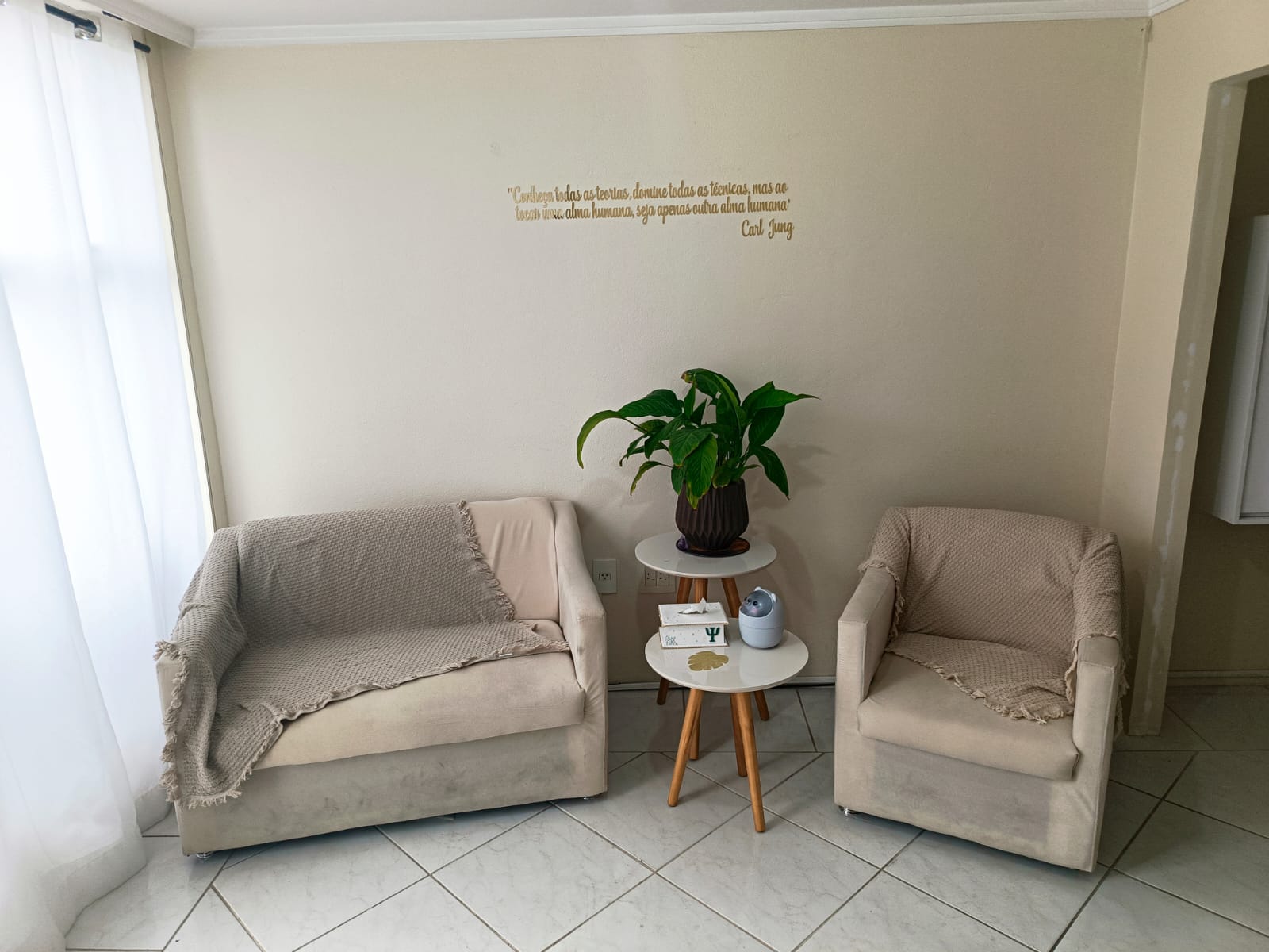 Sala de atendimento com poltronas bege, planta e citação de Carl Jung na parede